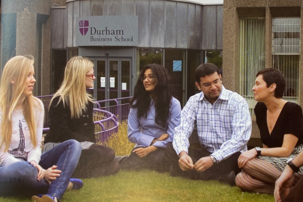 Mix of students sitting on the grass outside of business school