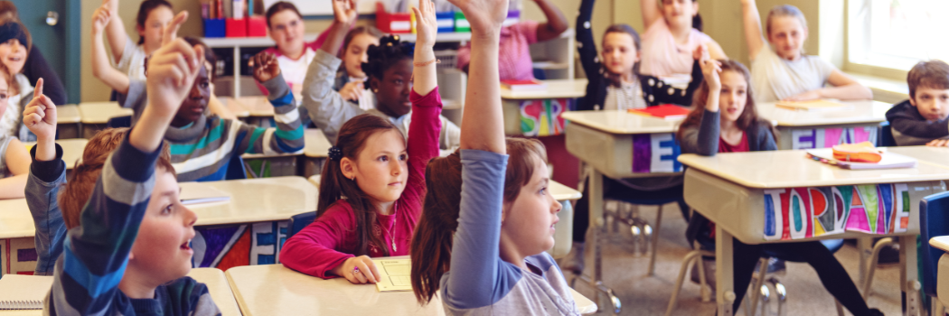 mix of students in a classroom raising their hands