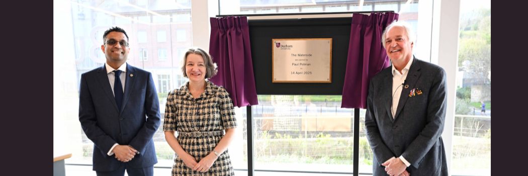 Three people standing in front of a plaque, revealed by a pulled curtain