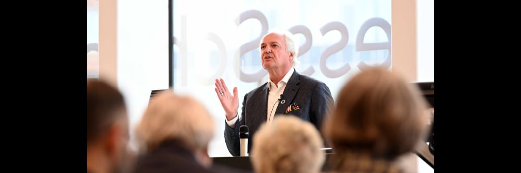 Man speaking to audience, backs of heads in foreground