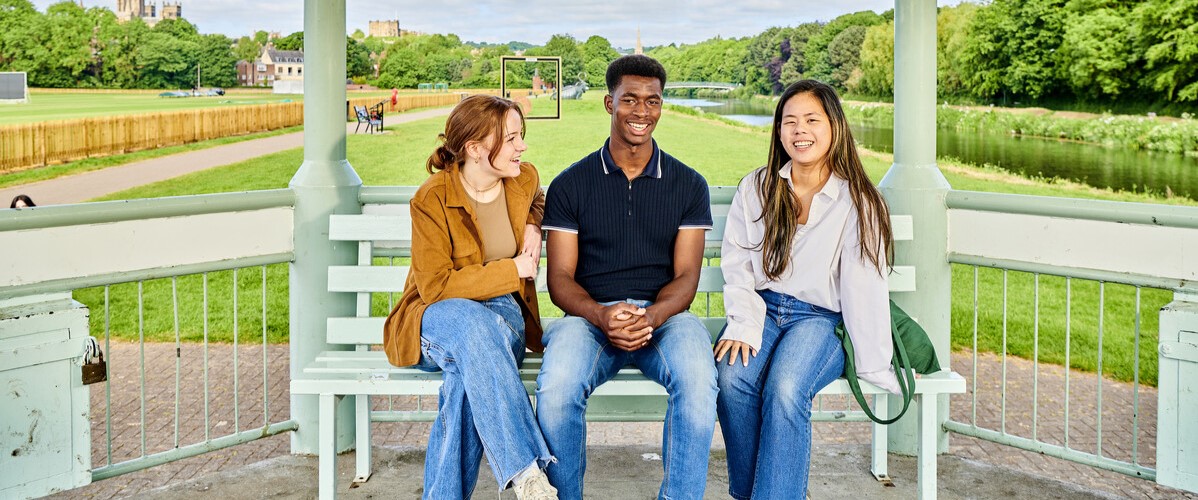 a diverse group of students sitting on a bench in front of a playing field