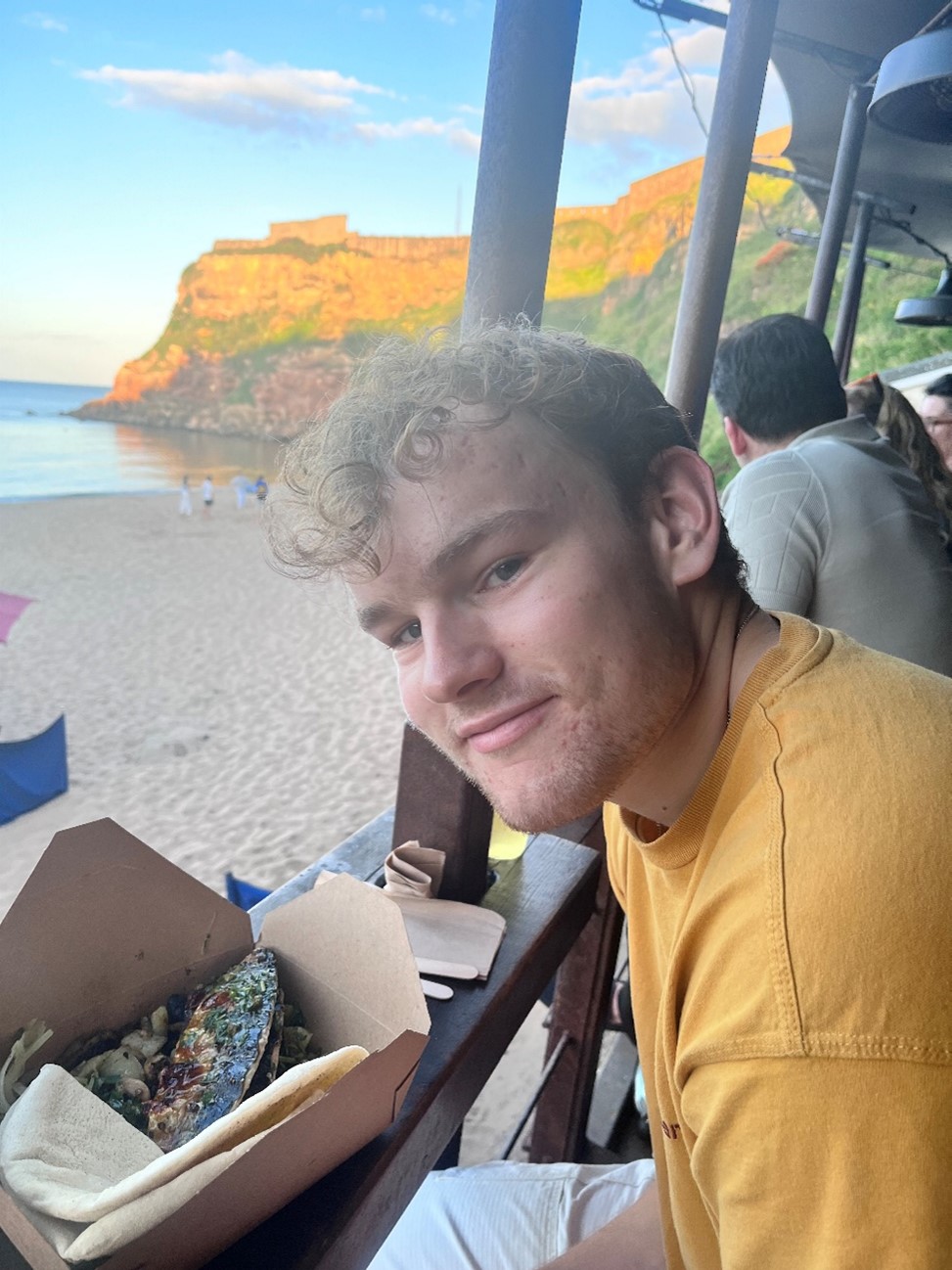 A Scholar sits on the beach at Tynemouth, with the cliffs in the background