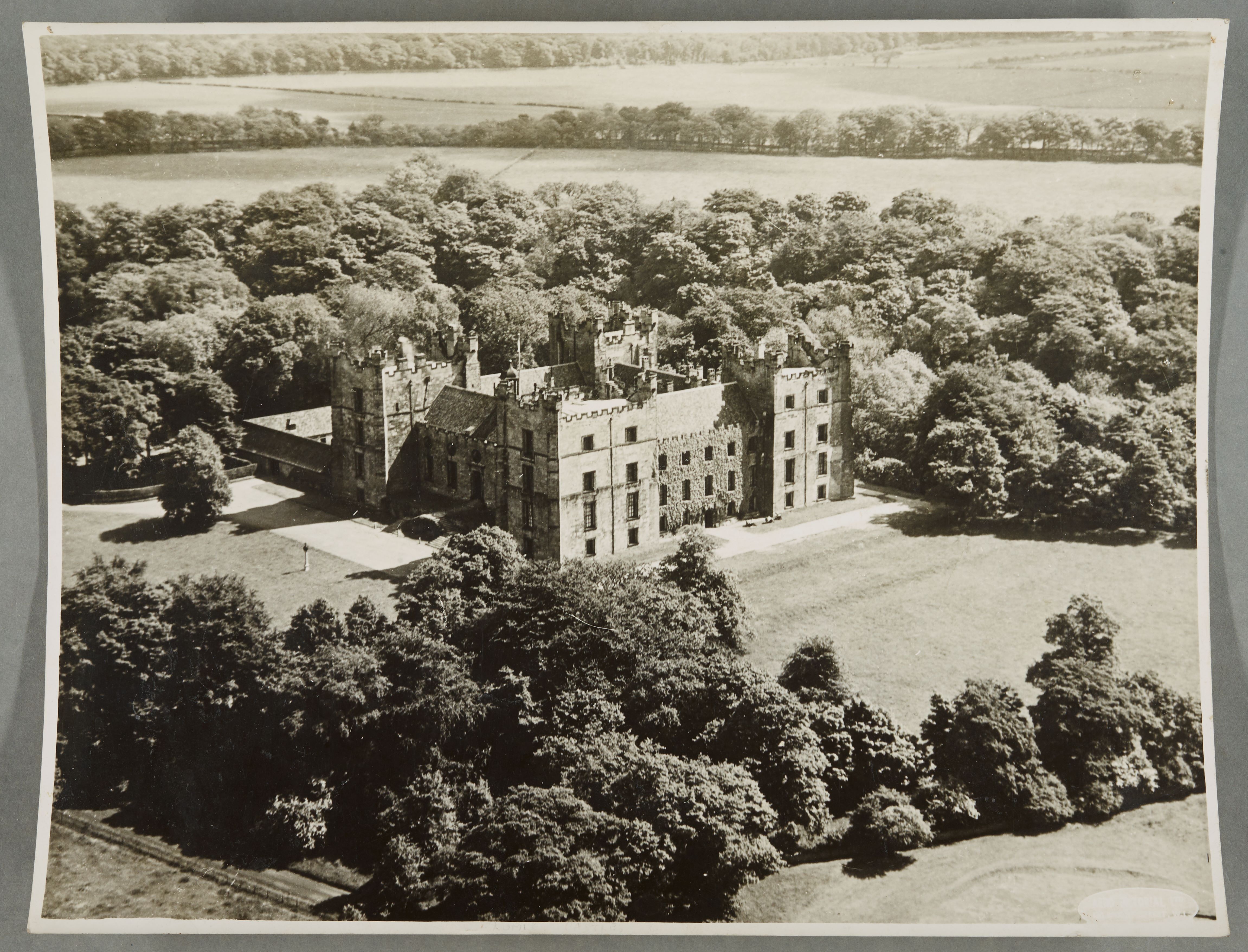 A view of Lumley Castle from the air, showing fields and trees surrounding it. Image is black and white.