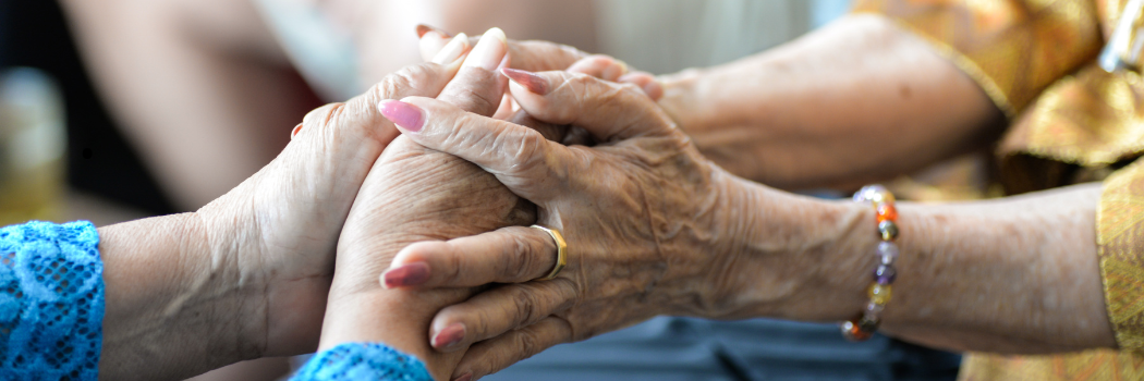 Close up of two older women's hands clasping each other.