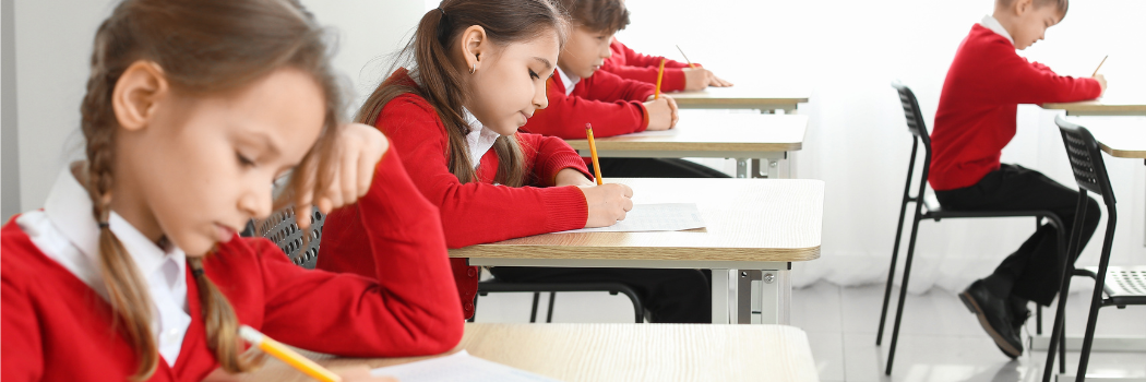 School pupils wearing red school uniform writing at desks in a classroom.