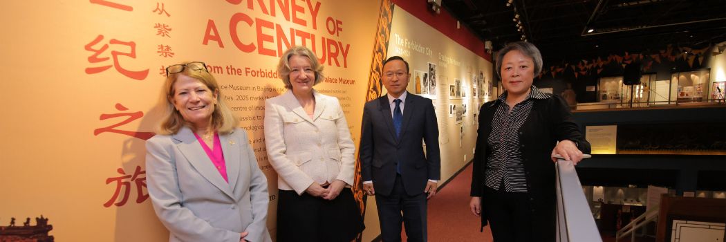 A group of people stand looking at the camera in front of a display board reading Journey of a Century