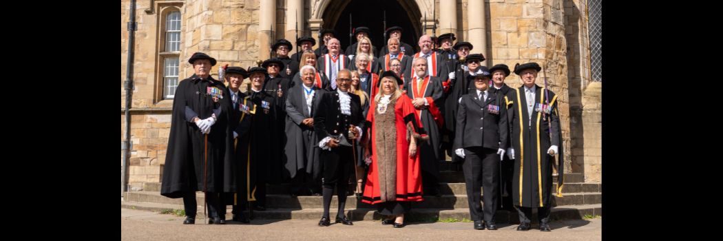 Men and women in traditional ceremonial dress standing on the steps of Durham Castle.