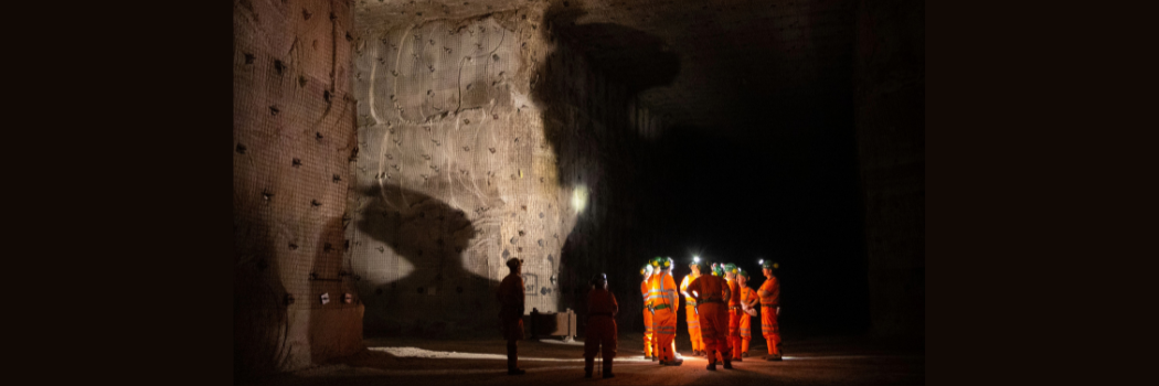 A group of people in a large cavern wearing orange jumpsuits and white helmets.