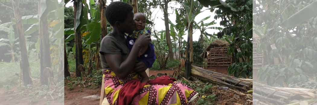A Ugandan mother in a bright dress sitting outside holding her baby