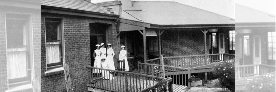 A black and white image from the early 1900s showing a group of nurses wearing white dresses outside a hospital.