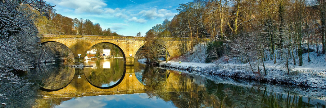 Winter sunlight shining on an arched bridge over the River Wear with snow on the riverbanks.