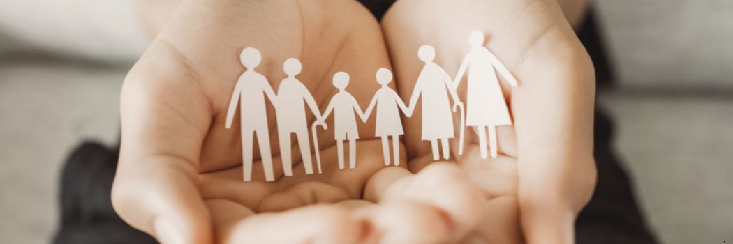 An paper cut out of an intergeneration family holding hands, sitting in the palms of a person's hands.