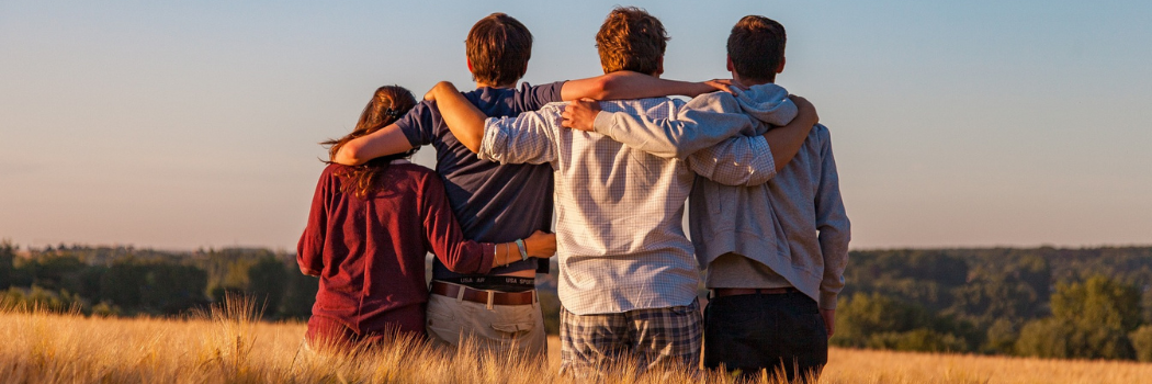 The backs of a group of teenagers with their arms around each others' shoulders standing outside.