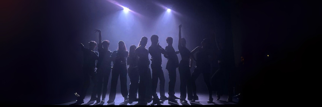 A mixed group of silhouettes in various poses standing under theatre lights surrounded by shadows