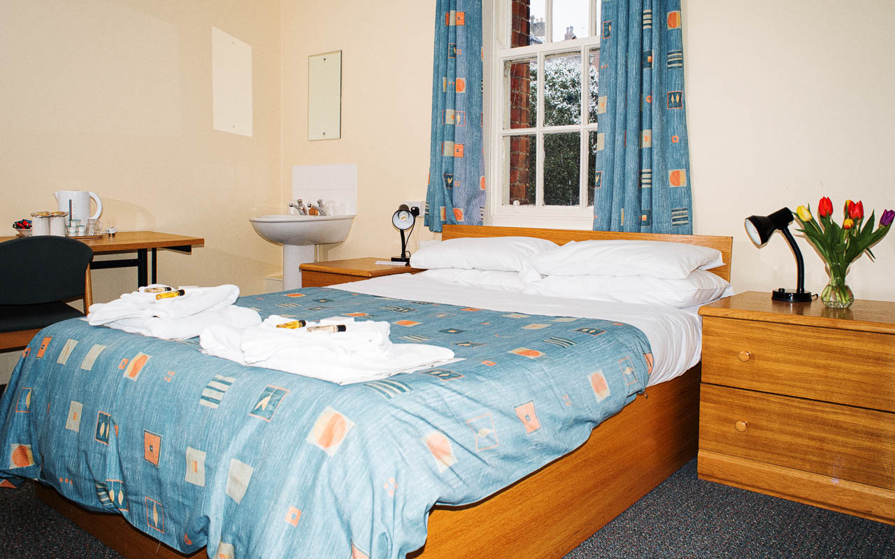 Student bedroom with a double bed, sink, table and set of drawers