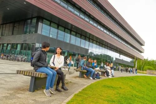 Slightly overcast day, with students sitting at wooden benches and tables outside the Maths and Computers Sciences Building