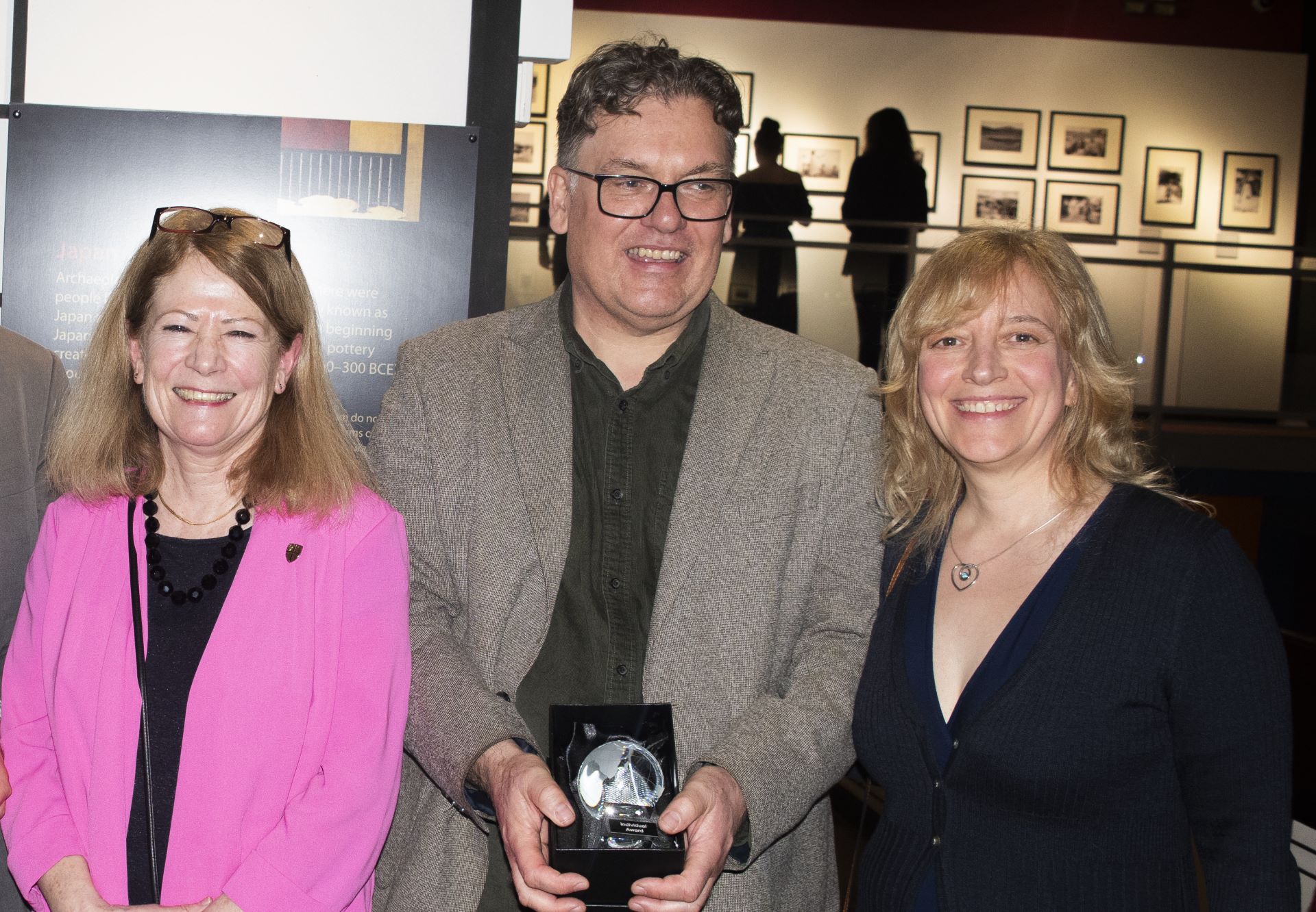 3 people smiling, one holding an award