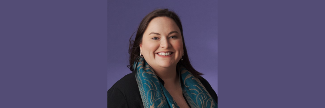 Woman with dark mid length hair wearing a jacket and scarf smiling