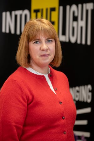 Alison standing in front of a logo that says Into the Light