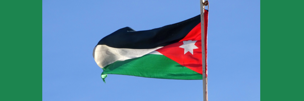 The flag of Jordan flies in front of a blue sky