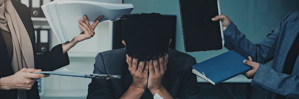 Overwhelmed business man in office surrounded by co workers