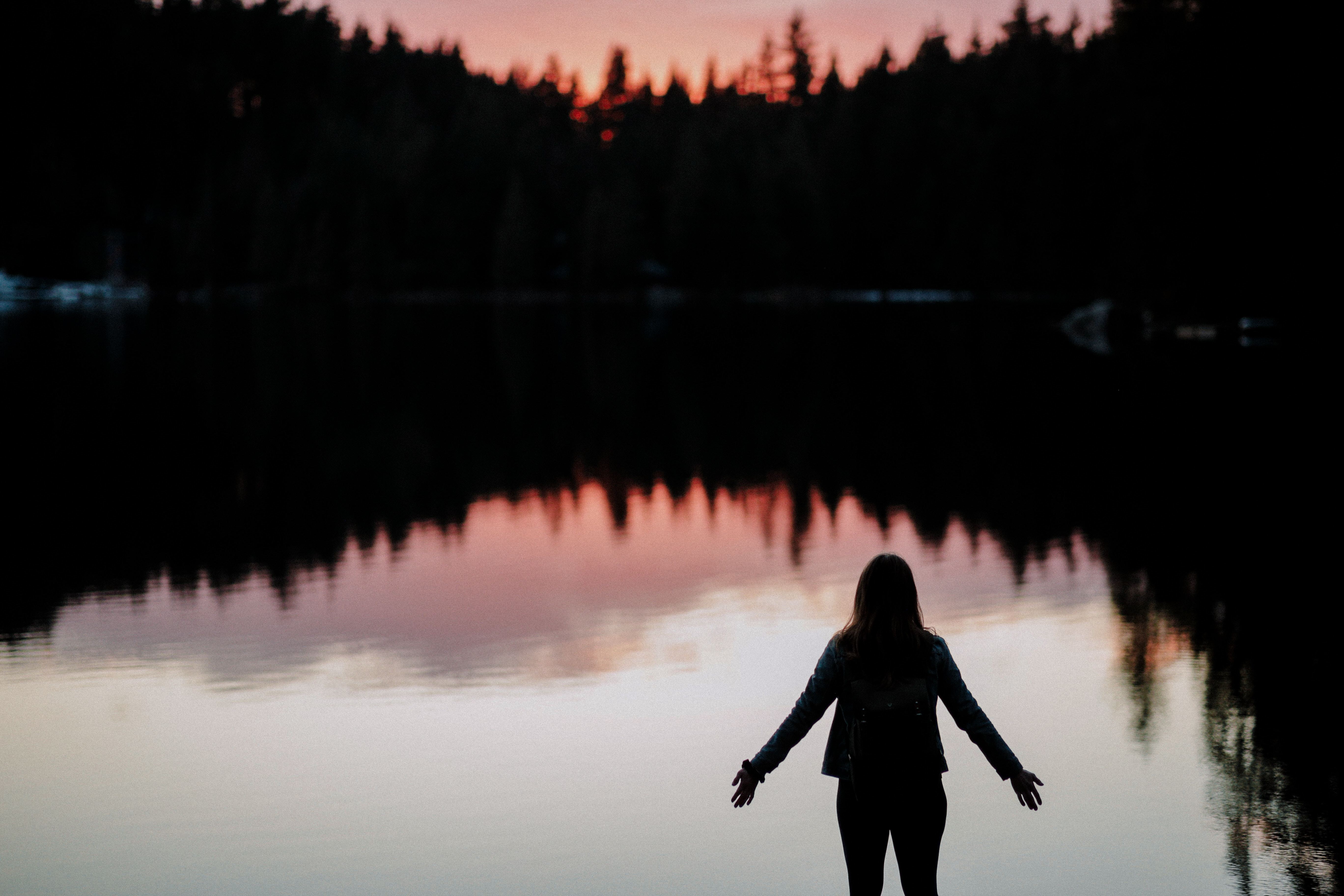 Silhouette of a person looking out on a lake surrounded by trees