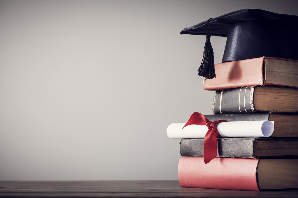Graduation hat, certificate and books on a desk