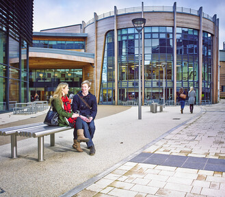 Two students sitting on a bench in front of the Palatine Centre.