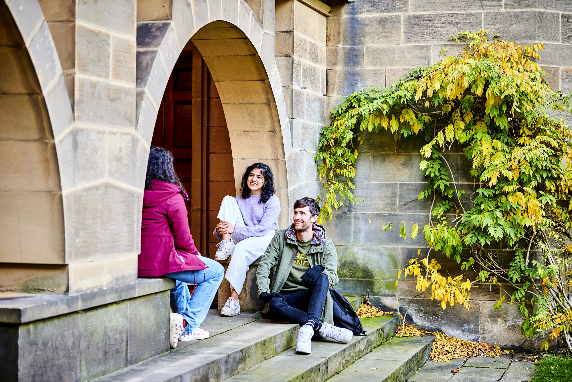Three students sat on stone steps underneath an archway