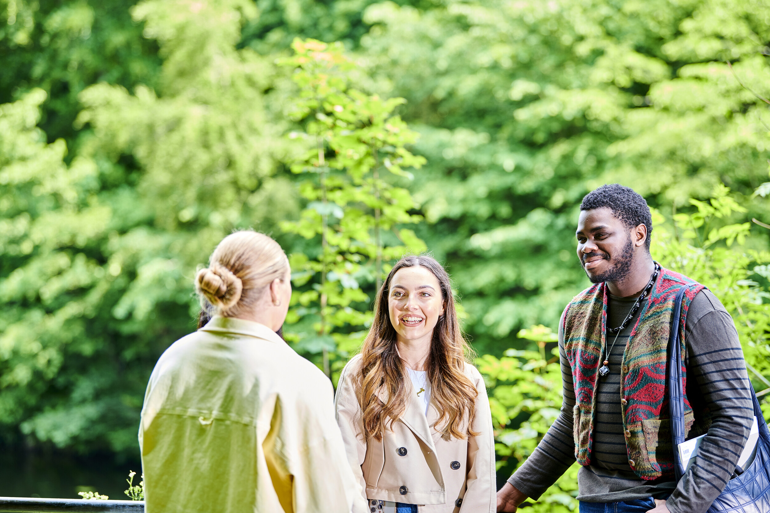 Three smiling students with foliage in the background