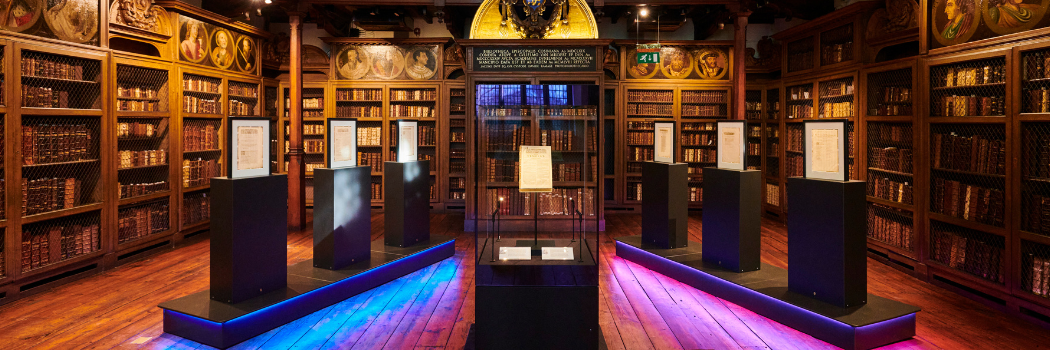 Durham Unviersity copy of William Shakespeare First Folio, on display in the centre of the image, with other display cases to the sides and vivid lighting underneath